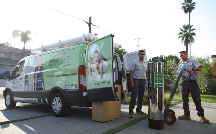 two men unloading water tank from a van